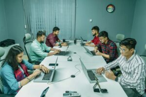 a group of people sitting around a table with laptops