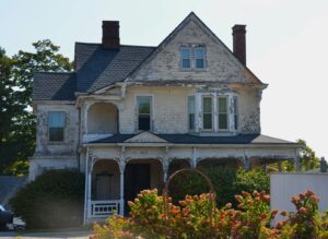 Old weathered house with peeling paint and overgrown bushes